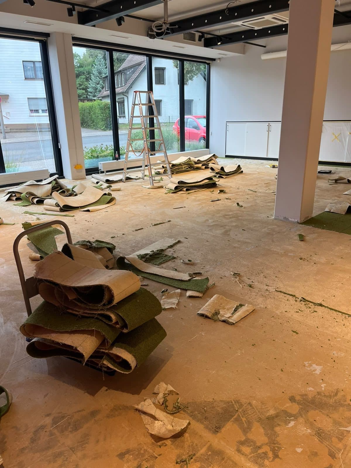 Alter grüner Teppichboden wird in einer Gewerbefläche herausgerissen und zur Entsorgung gestapelt